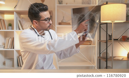 Diagnosis consultation. Online doctor. Smart medical specialist man explaining x ray of lungs disease at video appointment sitting in hospital office interior. 116780920