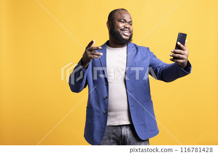 Joyful man having entertaining conversation with friends during teleconference meeting using cellphone, studio background. Jolly person having fun interacting with mates during online videocall 116781428