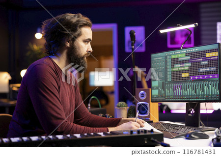 Songwriter taking notes to create new music in his home studio, writing down lyrics and harmonic elements before recording his song on daw software, acoustical engineering post production. Songwriter taking notes to create new music in his home studio, writing down lyrics and harmonic elements before recording his song on daw software, acoustical engineering post production. 116781431