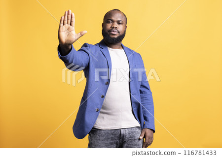Assertive african american man doing stop hand gesture sign. Annoyed BIPOC person doing firm halt sign gesturing, wishing to end concept, isolated over yellow studio background 116781433