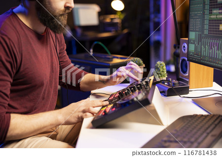 Music producer creating new tunes on mixing console by twisting pre amp knobs and adjusting volume levels in home studio. Artist songwriter working on post production with stereo gear. Music producer creating new tunes on mixing console by twisting pre amp knobs and adjusting volume levels in home studio. Artist songwriter working on post production with stereo gear. 116781438