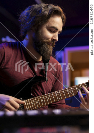 Songwriter playing new tunes on acoustic instrument in home studio, composing a new soundtrack with guitar accords. Young guitarist producing music with audio equipment and amplifier. Songwriter playing new tunes on acoustic instrument in home studio, composing a new soundtrack with guitar accords. Young guitarist producing music with audio equipment and amplifier. 116781446