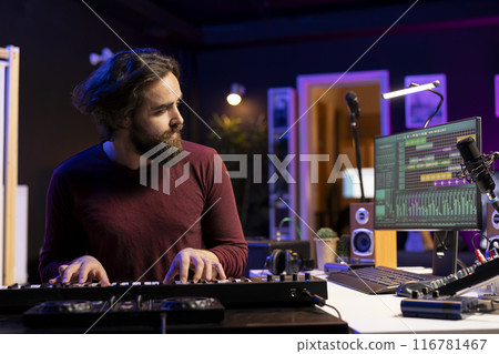 Music producer playing electronic piano keyboard in home studio, recording midi controller notes to create new songs. Young artist producing synthesizer keys, post production techniques. 116781467