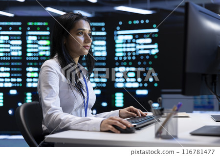 Indian woman doing yearly checkup to prolong data center electronics life span and avoid downtime. IT employee in server room monitoring server infrastructure components using PC Indian woman doing yearly checkup to prolong data center electronics life span and avoid downtime. IT employee in server room monitoring server infrastructure components using PC 116781477