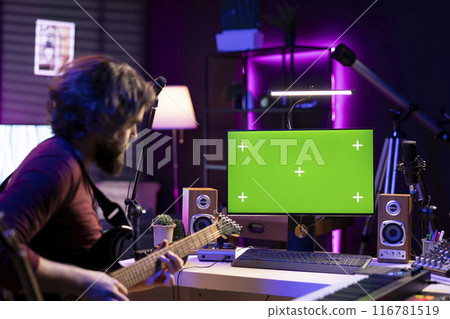 Young musician learning to play acoustic guitar with online lessons via computer with greenscreen layout in home studio. Audio engineer playing instrument to learn new accords, music industry. Young musician learning to play acoustic guitar with online lessons via computer with greenscreen layout in home studio. Audio engineer playing instrument to learn new accords, music industry. 116781519