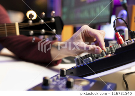 Audio engineer working with stereo equipment and control panel board, mixing and mastering tunes in his home studio. Composer singer recording soundtracks and editing in post production. Close up. Audio engineer working with stereo equipment and control panel board, mixing and mastering tunes in his home studio. Composer singer recording soundtracks and editing in post production. Close up. 116781540