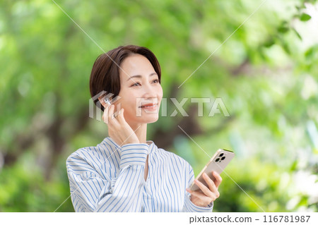 Woman listening to music with earphones, fresh greenery 116781987