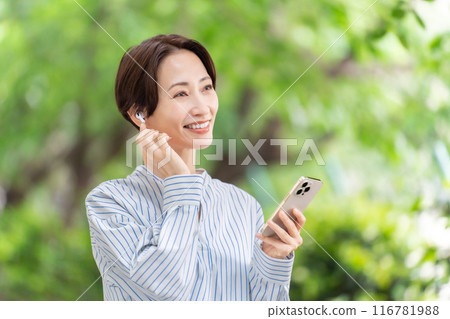 Woman listening to music with earphones, fresh greenery 116781988