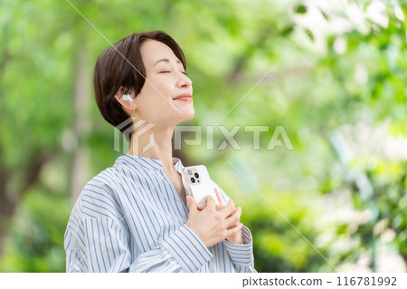 Woman listening to music with earphones, fresh greenery Woman listening to music with earphones, fresh greenery 116781992