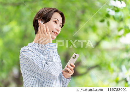 Woman listening to music with earphones, fresh greenery 116782001