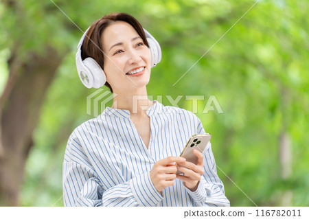 Woman listening to music with headphones, fresh greenery 116782011