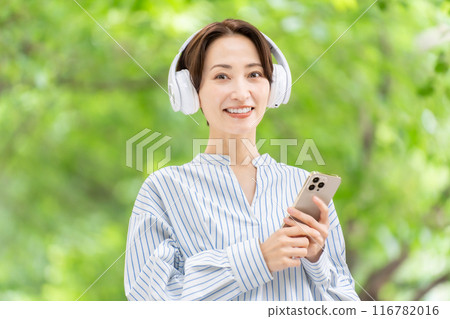 Woman listening to music with headphones, fresh greenery 116782016