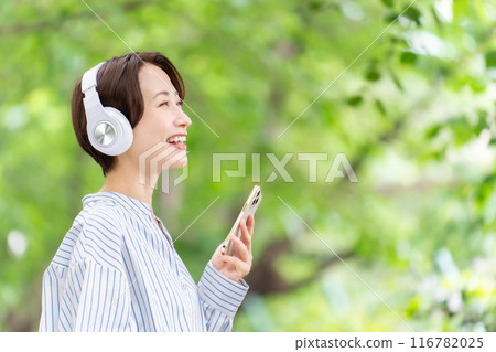 Woman listening to music with headphones, fresh greenery 116782025