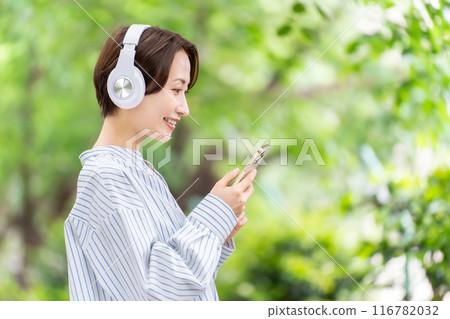 Woman listening to music with headphones, fresh greenery 116782032