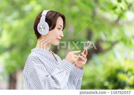 Woman listening to music with headphones, fresh greenery Woman listening to music with headphones, fresh greenery 116782037