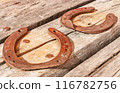 Two old vintage and rusty horseshoes are nailed to a dried and cracked piece of wood. 116782756