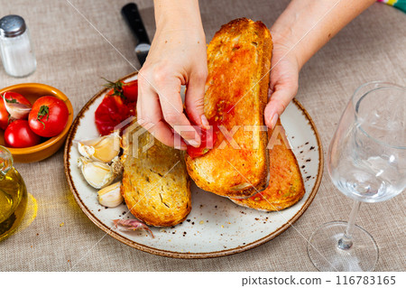 Female hands rubbing toast with tomato while preparing Pan Con Tomate 116783165