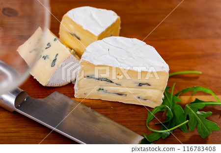 Whole wheel of piquant creamy blue cheese on cutting board Whole wheel of piquant creamy blue cheese on cutting board 116783408