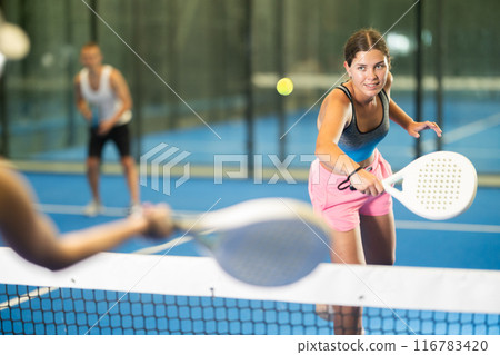 Girl paired with a man plays padel on an indoor tennis court 116783420