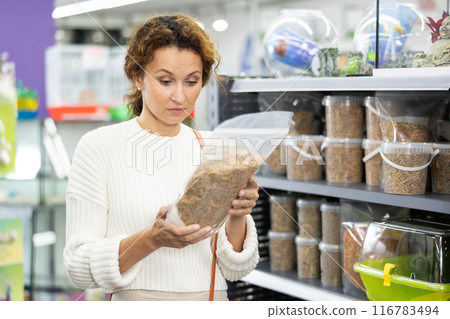Young woman in animal goods store examines packaging of dry food for turtles 116783494