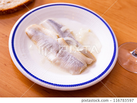 On wooden table is plate with appetizer - salted Atlantic herring fillet with pickled onions 116783597