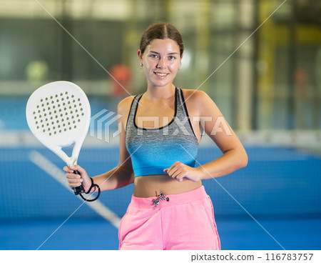 Young woman posing indoor on padel court with racket and ball 116783757