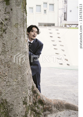 A man peeking out from behind a tree 116783813