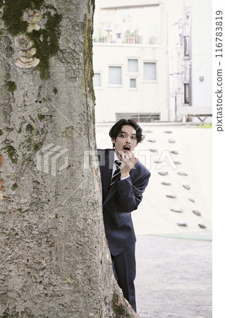 A man peeking out from behind a tree 116783819