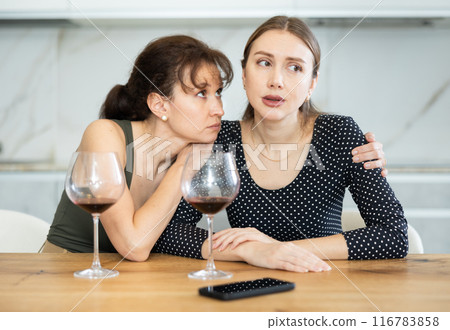 Sad woman sits silently in kitchen, friend sympathize and comfort her 116783858