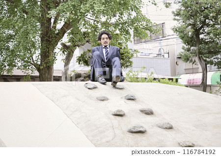 A man in a suit sitting on a playground equipment in a park 116784192