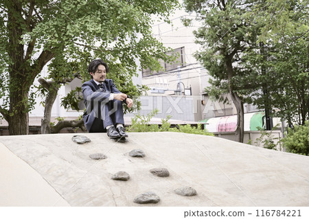 一個穿著西裝的男人坐在公園的遊樂場設備上 一個穿著西裝的男人坐在公園的遊樂場設備上 116784221
