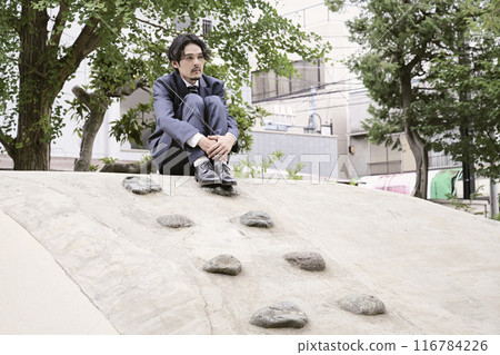 A man in a suit sitting on a playground equipment in a park 116784226