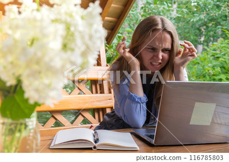 Stressed Young woman freelancer working online using laptop outdoors in garden. Emotional stress anxiety, homelife difficulties. Online meeting 116785803
