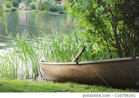 Old wooden boat with oars on lake shore. Houses and buildings. Water transportation and nature in summer.  116786201