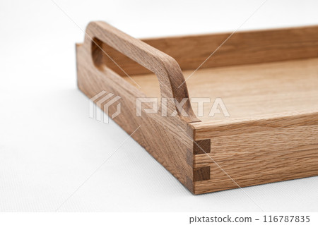 Elegant solid oak wood tray with dovetail joints and carved handles on the sides for easy carrying closeup view on white background Elegant solid oak wood tray with dovetail joints and carved handles on the sides for easy carrying closeup view on white background 116787835