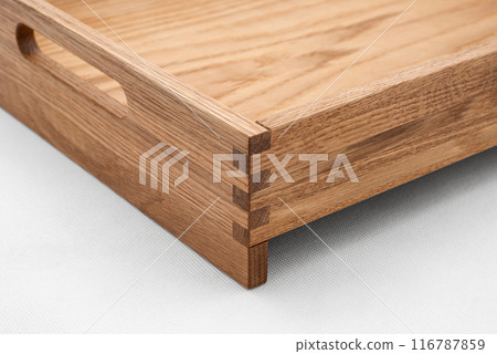 Solid oak wood tray with dovetail joints and cutout handles on the sides for easy carrying closeup view on white background 116787859