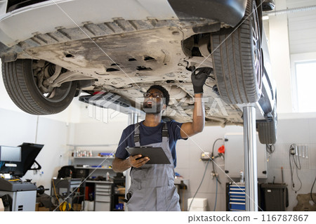 Mechanic inspecting car undercarriage at auto repair shop Mechanic inspecting car undercarriage at auto repair shop 116787867