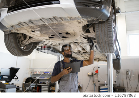 Mechanic inspecting car undercarriage in auto repair shop Mechanic inspecting car undercarriage in auto repair shop 116787868