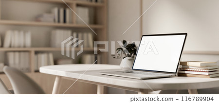 A close-up image of a laptop computer with a white-screen mockup on a table in a contemporary room. 116789904