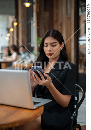 An attractive Asian businesswoman is using her smartphone while working remotely from a cafe. An attractive Asian businesswoman is using her smartphone while working remotely from a cafe. 116790039