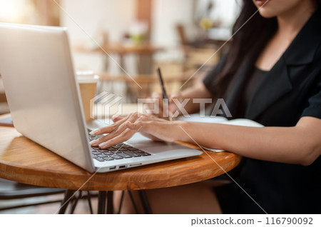 A businesswoman working remotely from a cafe, typing on the laptop keyboard and taking note. 116790092