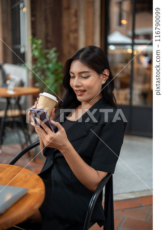 An Asian woman is sipping coffee and replying chat on her smartphone while relaxing in a coffee shop An Asian woman is sipping coffee and replying chat on her smartphone while relaxing in a coffee shop 116790099