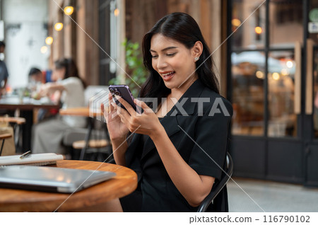 A confident Asian businesswoman is smiling at her phone, reading messages on her smartphone. 116790102