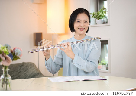 Middle-aged woman playing the flute in the living room 116791787