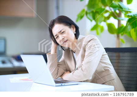 Middle-aged woman showing signs of fatigue in the office Middle-aged woman showing signs of fatigue in the office 116791789