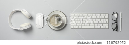 A cup of coffee with headphones and a keyboard on a light background A cup of coffee with headphones and a keyboard on a light background 116792952