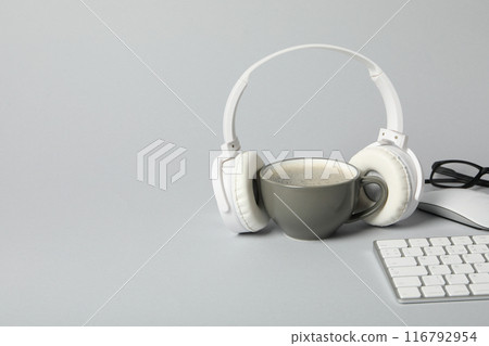 A cup of coffee with headphones and a keyboard on a light background A cup of coffee with headphones and a keyboard on a light background 116792954