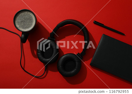 A black cup of tea with headphones and a notebook on a red background A black cup of tea with headphones and a notebook on a red background 116792955