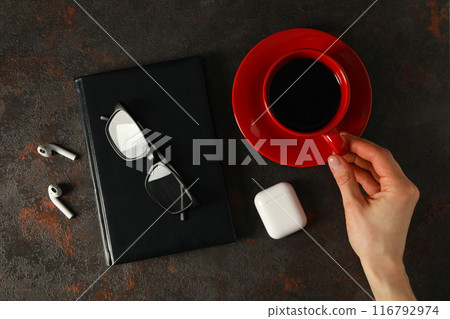 A cup of coffee with headphones and a notebook on a dark background 116792974