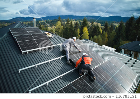 Electricians building photovoltaic solar module station on roof of house. Men technicians in helmets installing solar panel system outdoors. Concept of alternative and renewable energy. Aerial view. 116793151